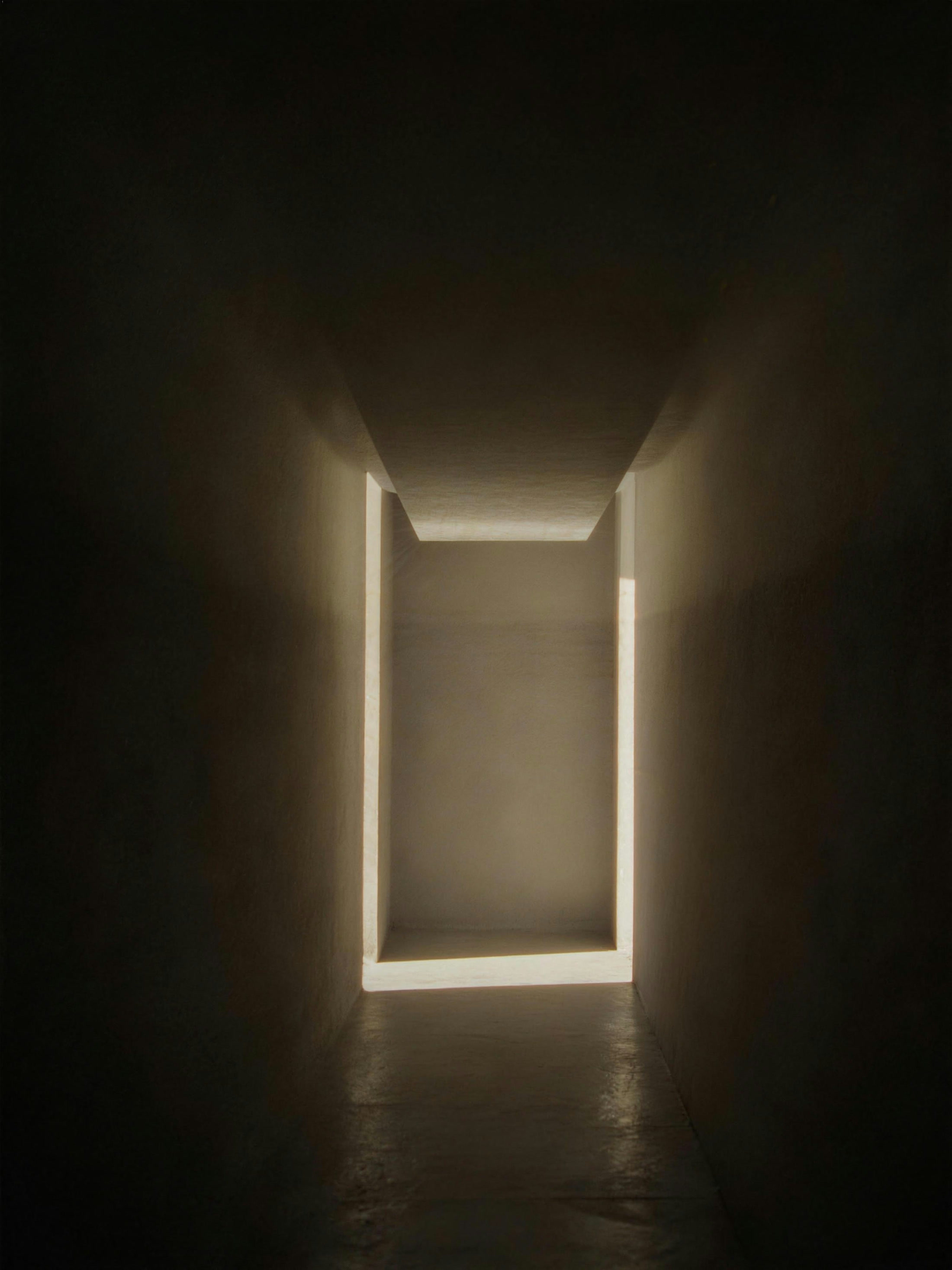 A dark corridor with a vertical slot of warm daylight falling across plaster walls
